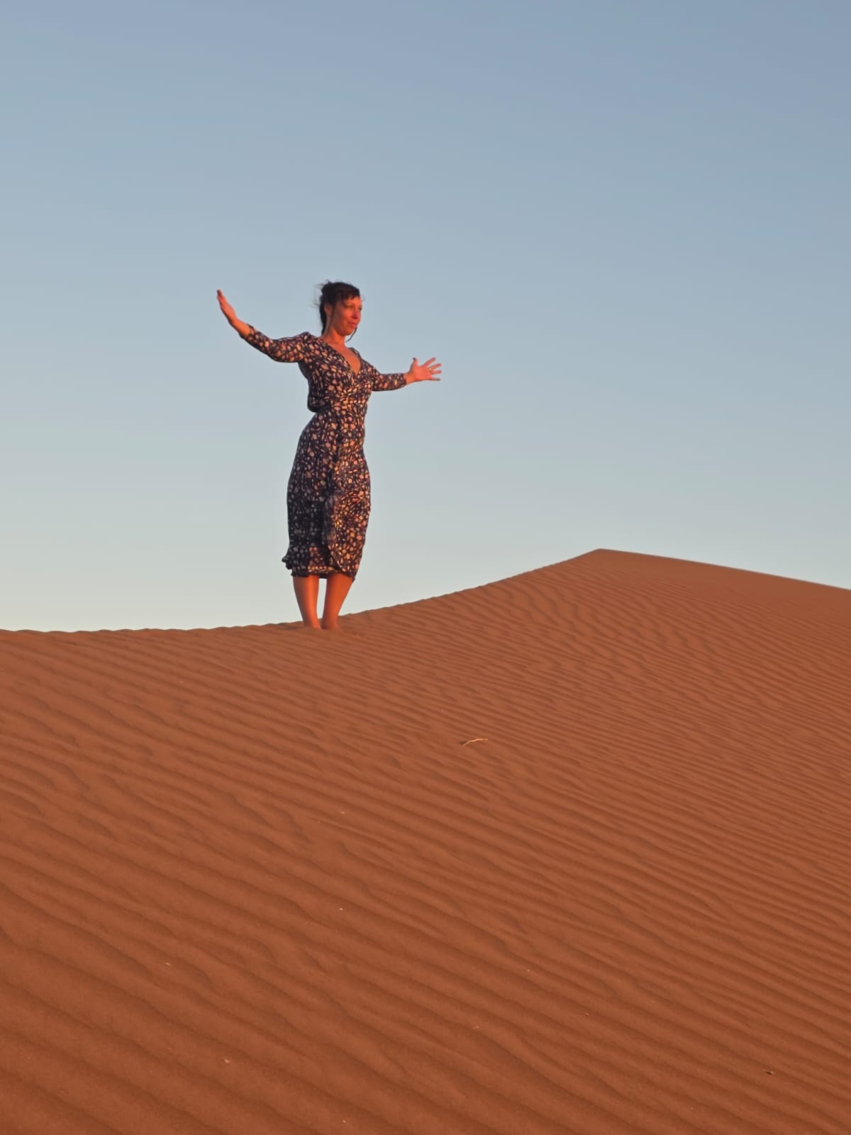 Dana standing with open arms on a dune