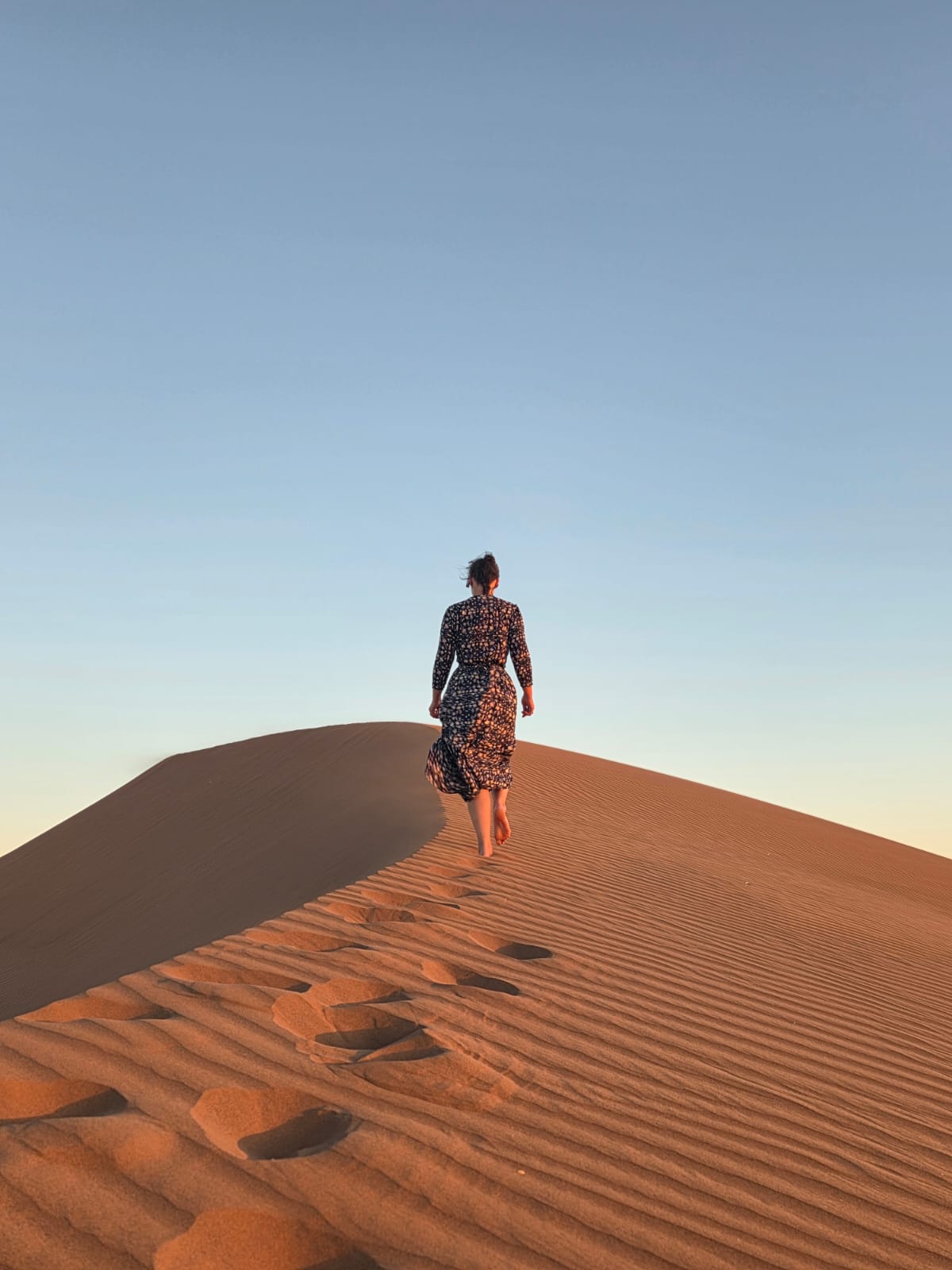 Dana walking barefoot along the crest of a sand dune