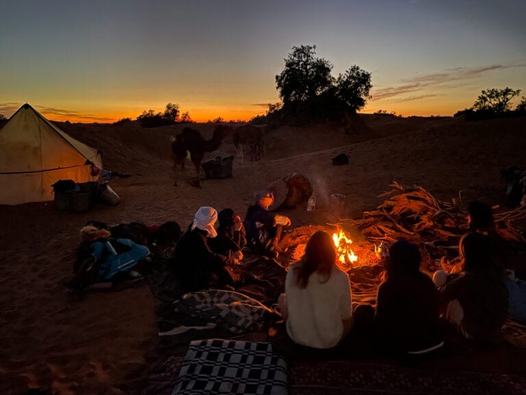 The group sitting together by the fire at dusk